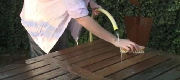 Washing a timber table with a water hose and brush